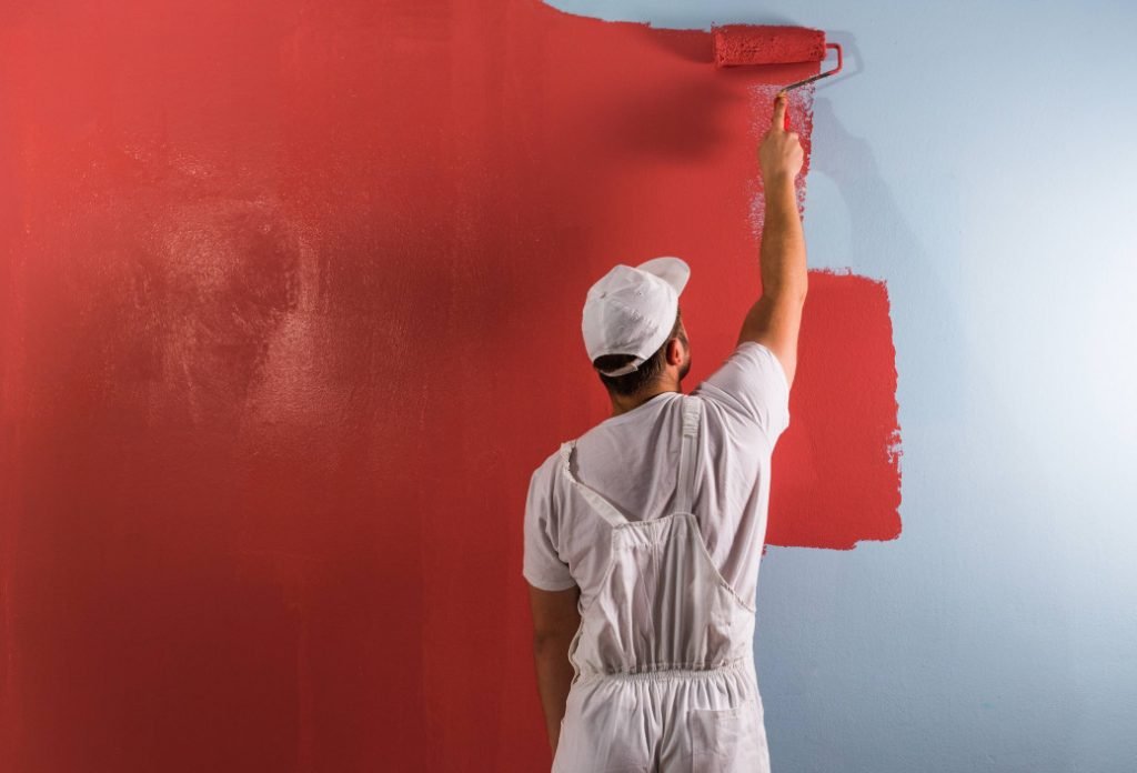 A man applies red paint to a wall, showcasing a professional painting service in action.